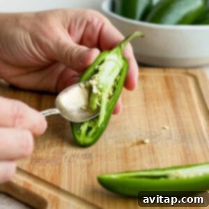 A person cutting a jalapeno pepper with a spoon, removing seeds and pith.