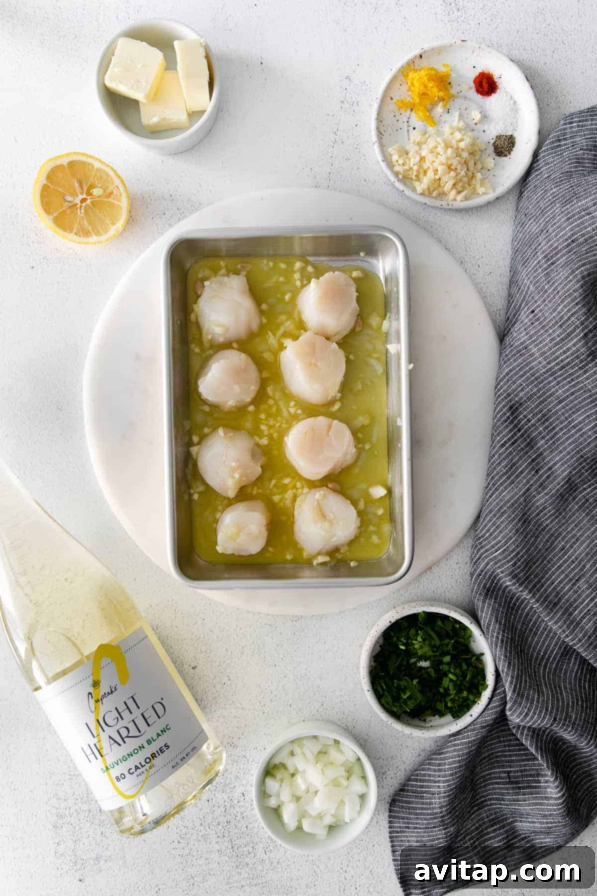 Scallops marinating in a bowl with lemon slices and herbs.