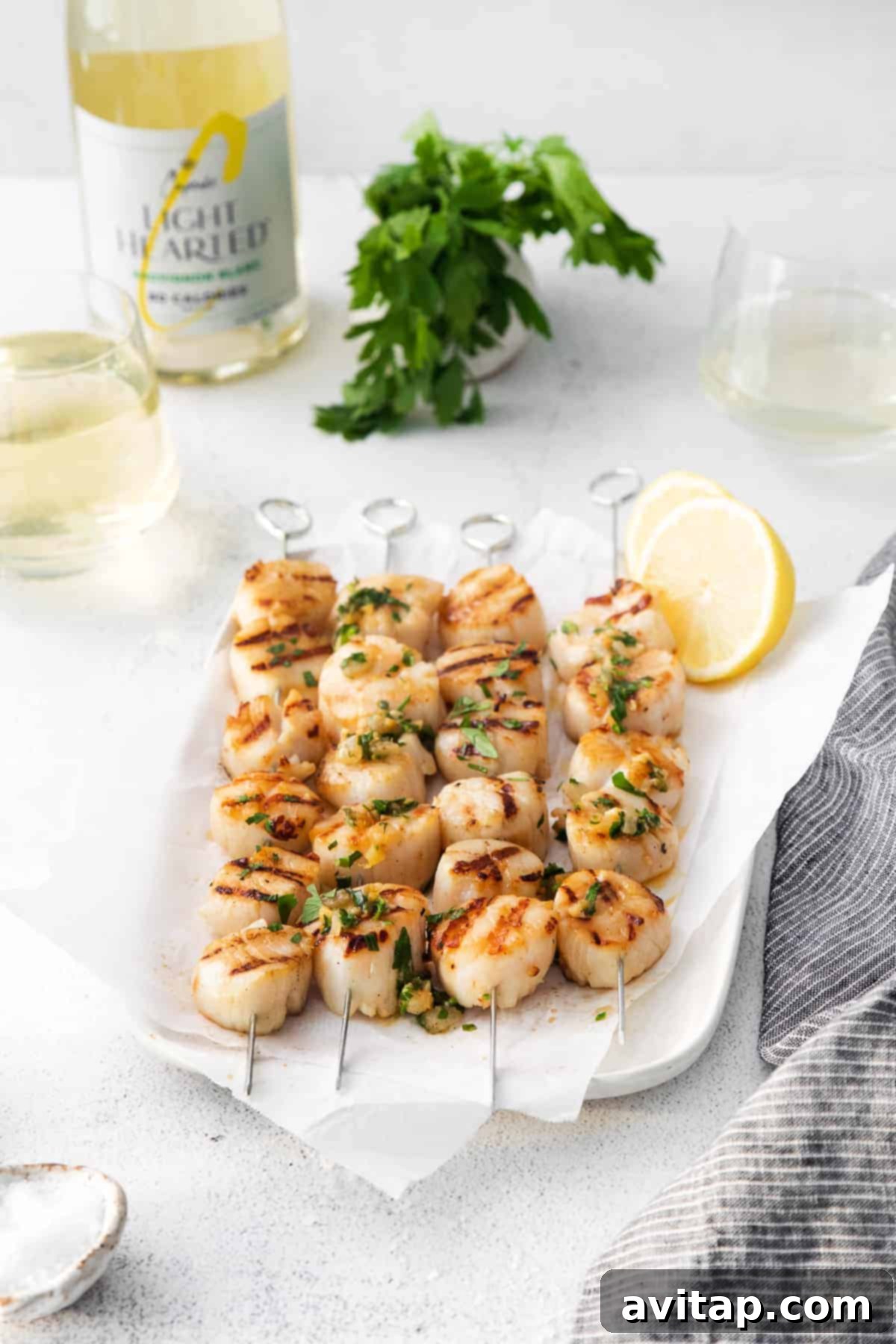 Grilled scallops artfully arranged on a plate with fresh herbs and lemon.