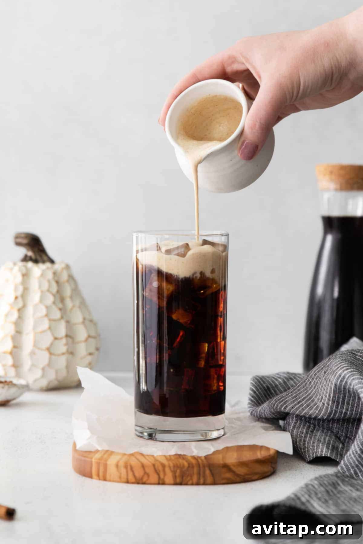 Velvet Pumpkin Cold Brew 5 Hands pouring rich pumpkin cream over dark cold brew coffee and ice in a tall glass, creating a beautiful swirl of colors.