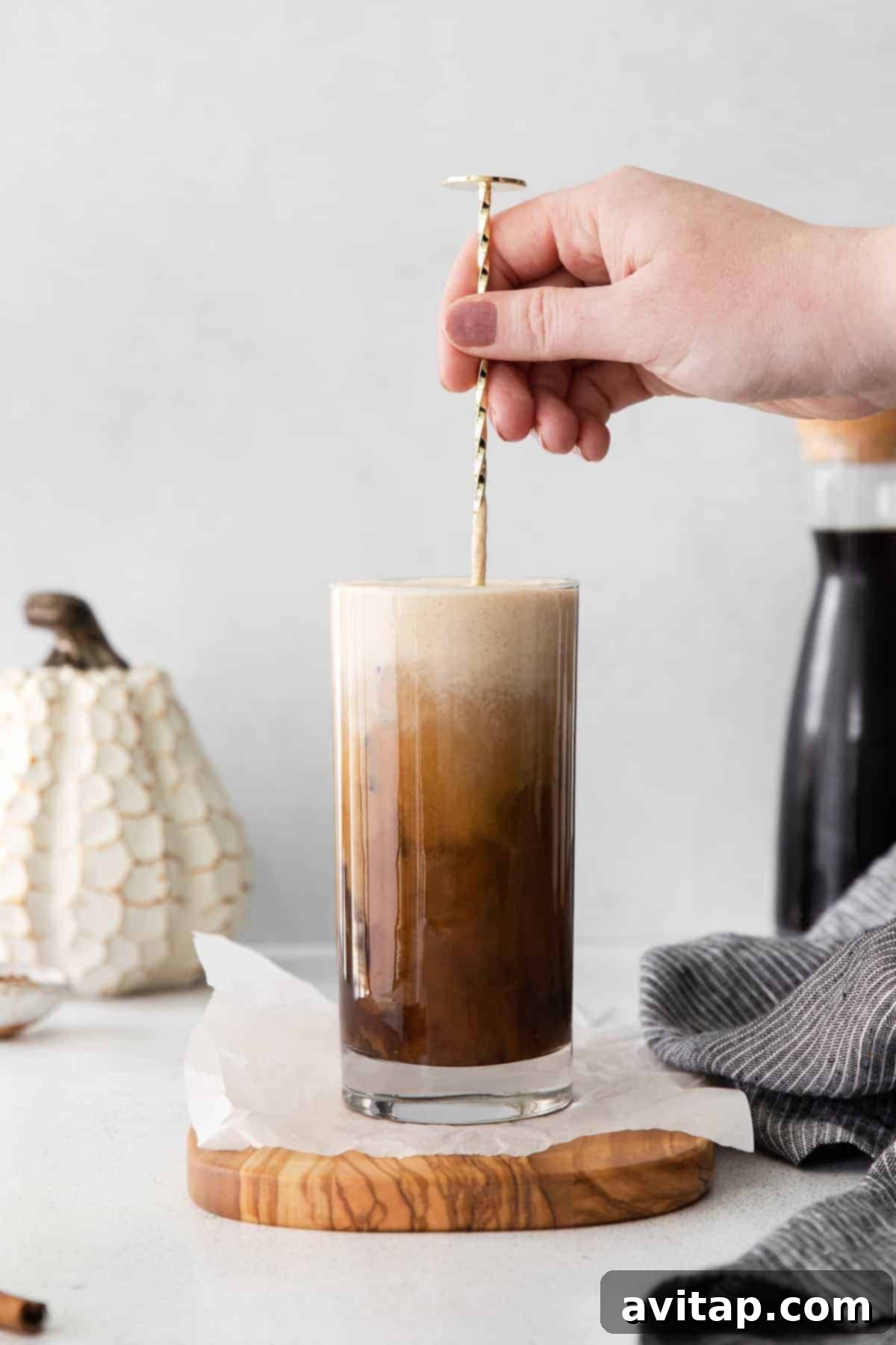 Velvet Pumpkin Cold Brew 6 A hand stirring a glass of Pumpkin Cream Cold Brew with a straw, blending the creamy top layer with the coffee.