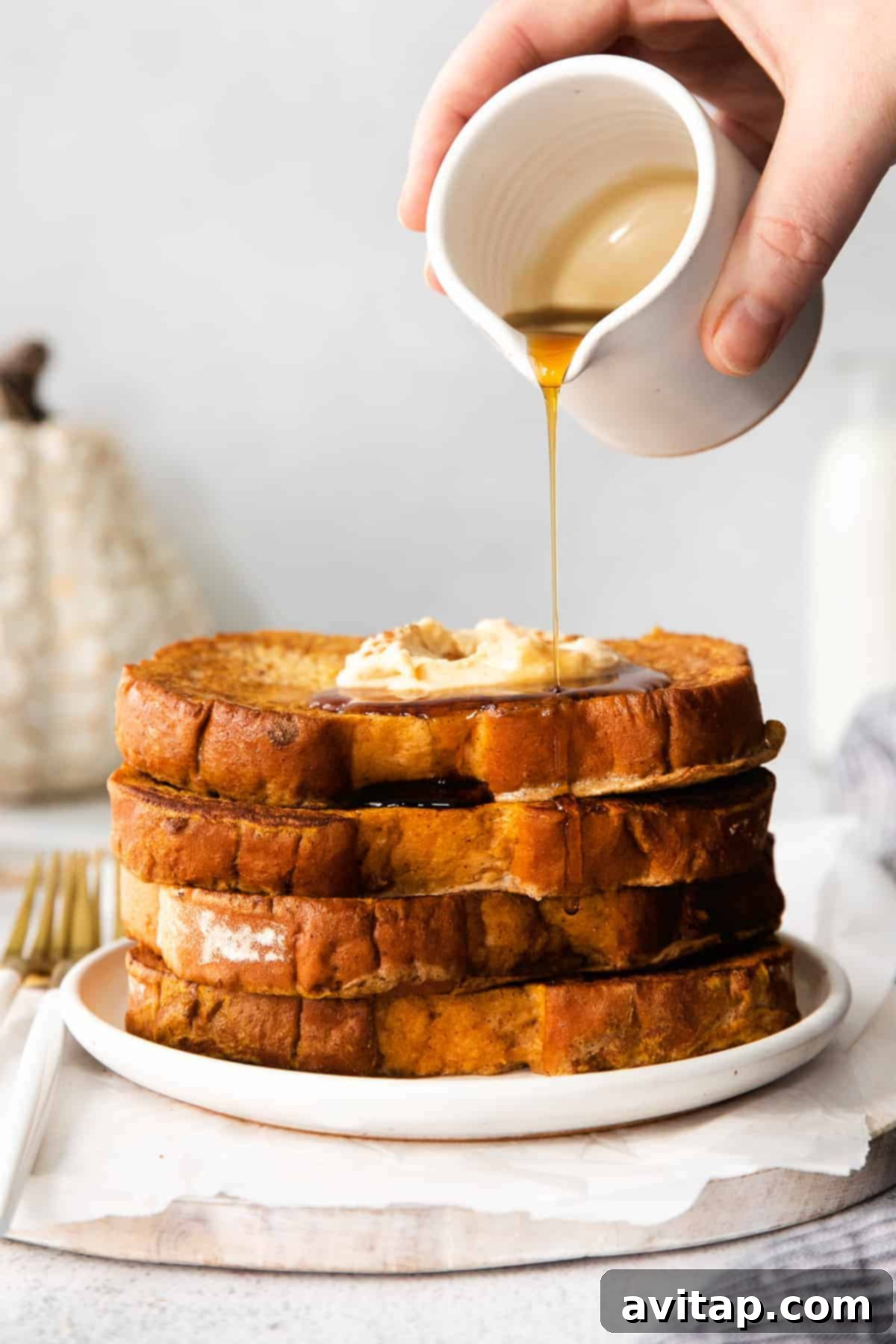 Pouring maple syrup over pumpkin french toast, garnished with a dusting of cinnamon and a dollop of whipped cream.