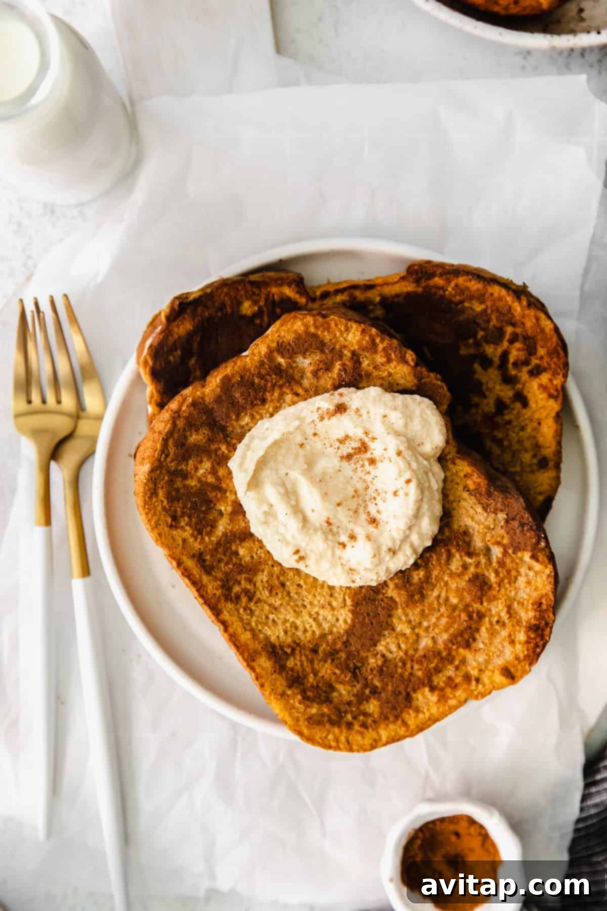 Pumpkin french toast topped with a generous swirl of coconut whipped cream and a drizzle of maple syrup.