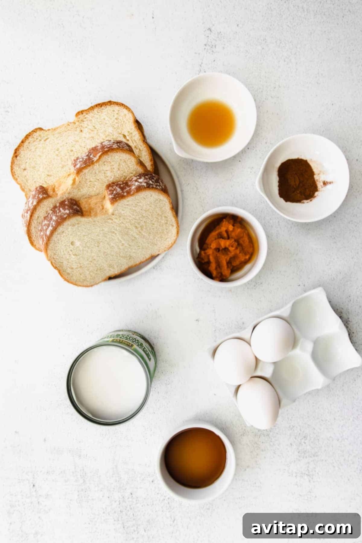 All the ingredients for pumpkin french toast laid out in small bowls on a kitchen counter, ready for preparation.