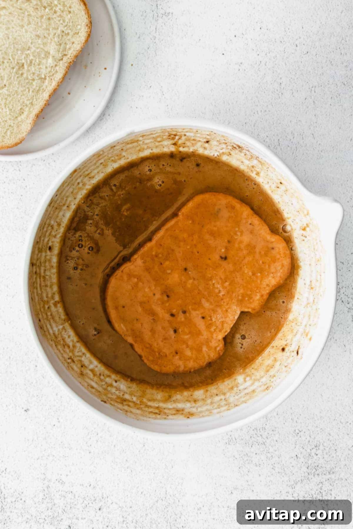 Slices of bread soaking in a pumpkin-infused egg mixture in a bowl, ready for cooking.
