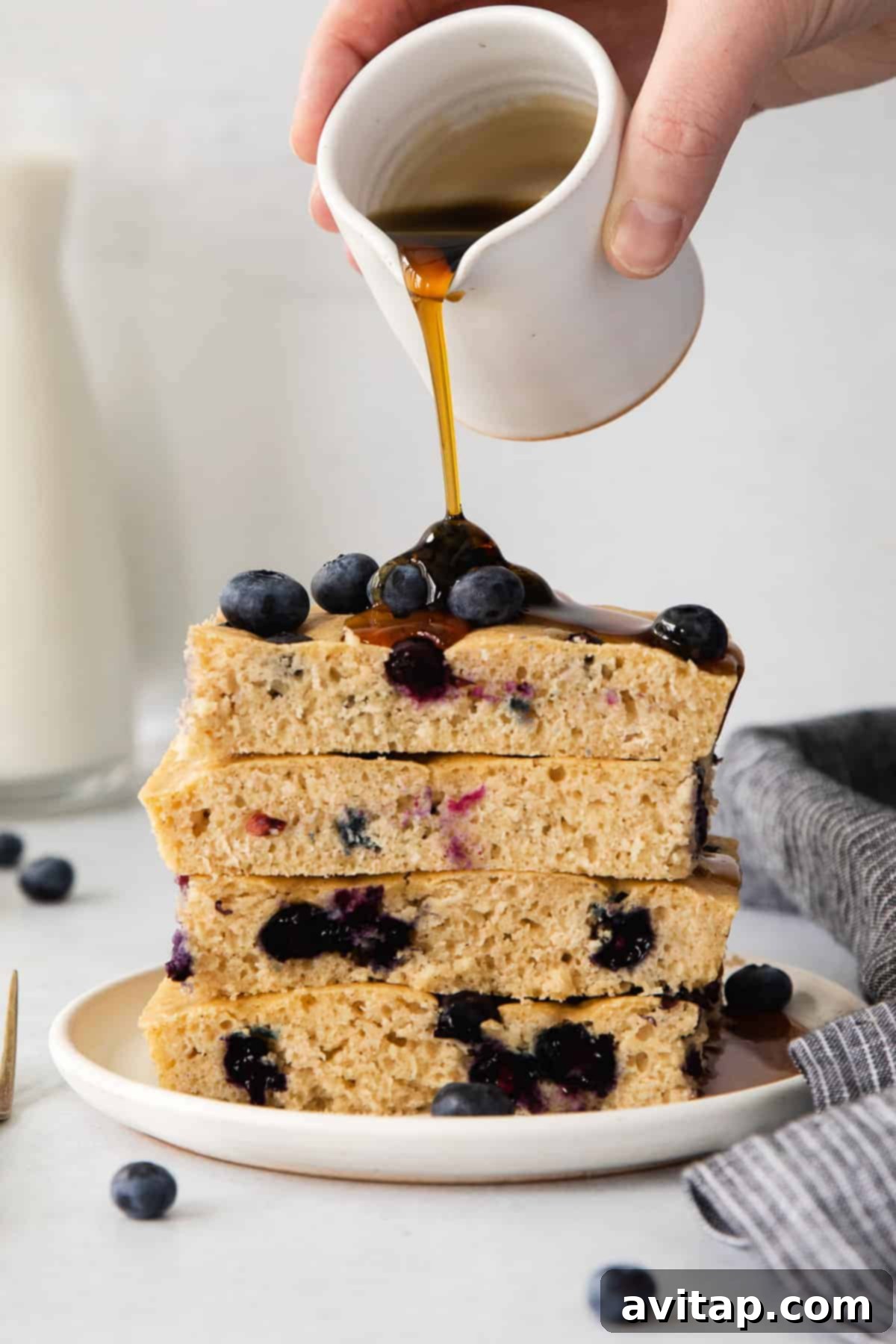 Pouring maple syrup over freshly baked sheet pan pancakes topped with fresh fruit.