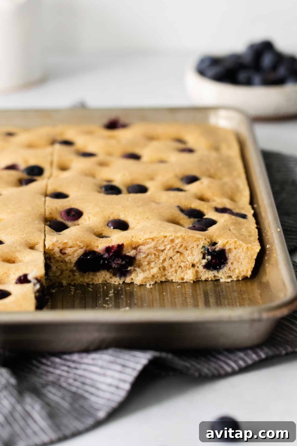 A sheet pan filled with golden, blueberry-studded pancakes on a kitchen counter.