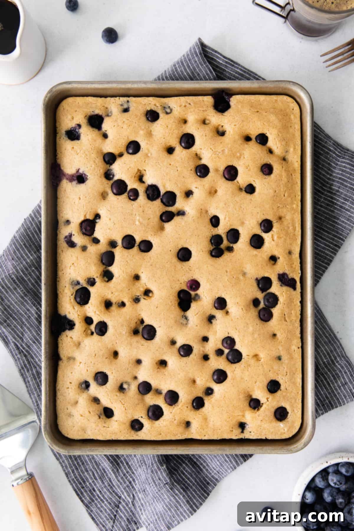 Freshly baked sheet pan pancakes topped with blueberries, cut into squares on a cooling rack.