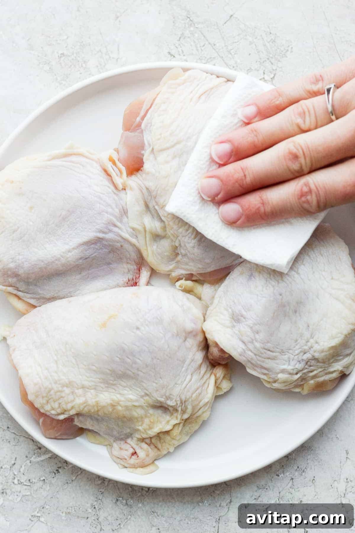Piled chicken thighs on a cutting board, ready for seasoning, highlighting the importance of a dry surface for optimal crispiness. Chicken thighs being patted dry with a paper towel before seasoning, a critical step for crispy skin.
