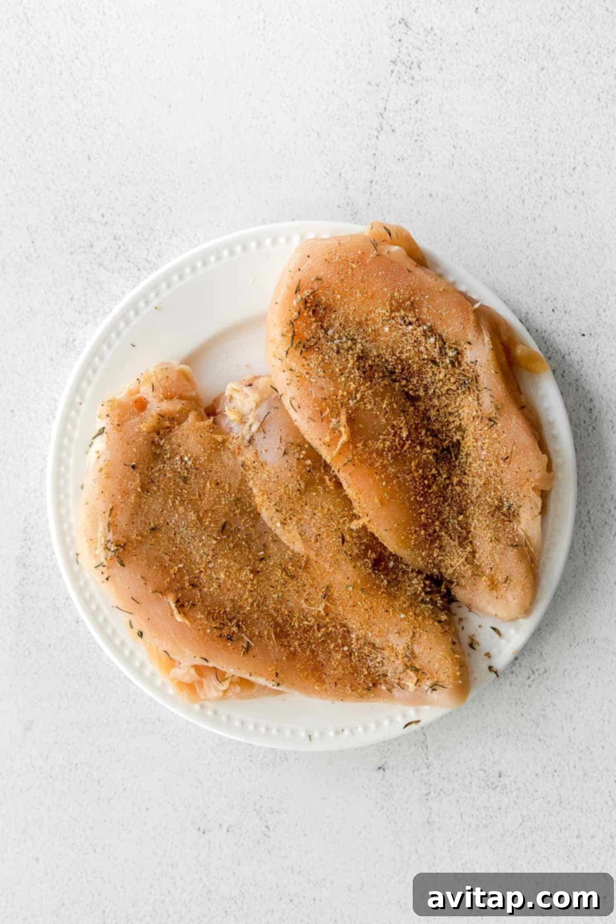 Seasoned raw chicken breast on a plate, ready for the air fryer.