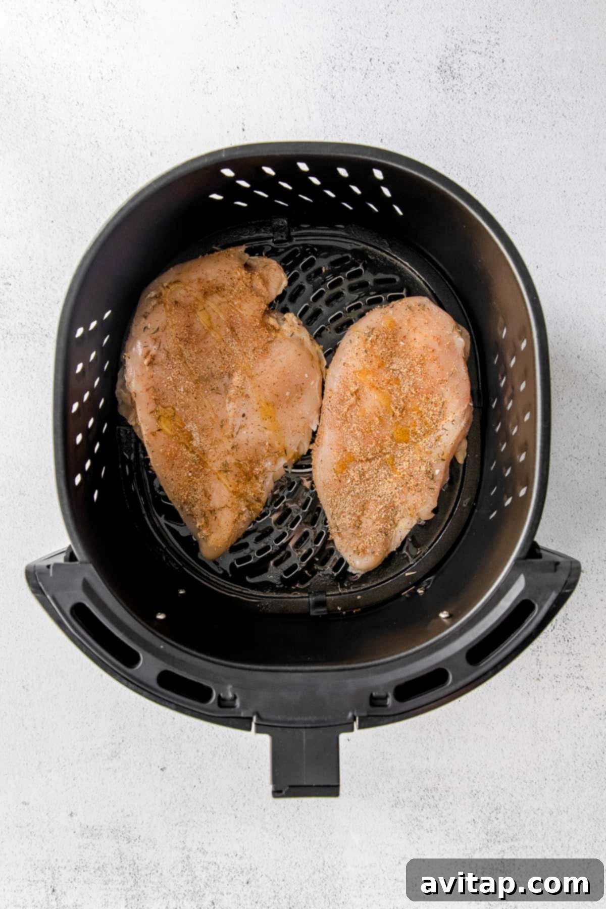 Raw chicken breasts nestled in an air fryer basket, ready for cooking.