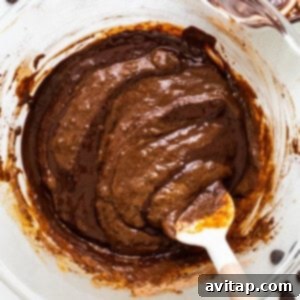 A bowl of chocolate pudding-like batter with a wooden spoon, showing the folded-in melted chocolate.