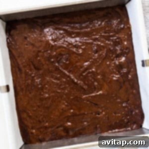 A pan ready for baking, filled with chocolate cake batter, next to a small bowl of extra chocolate chips for topping.