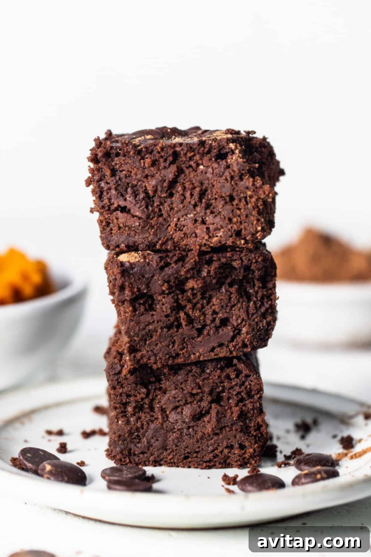 A beautifully arranged stack of freshly baked brownies rests on a pristine white plate, showcasing their rich texture.