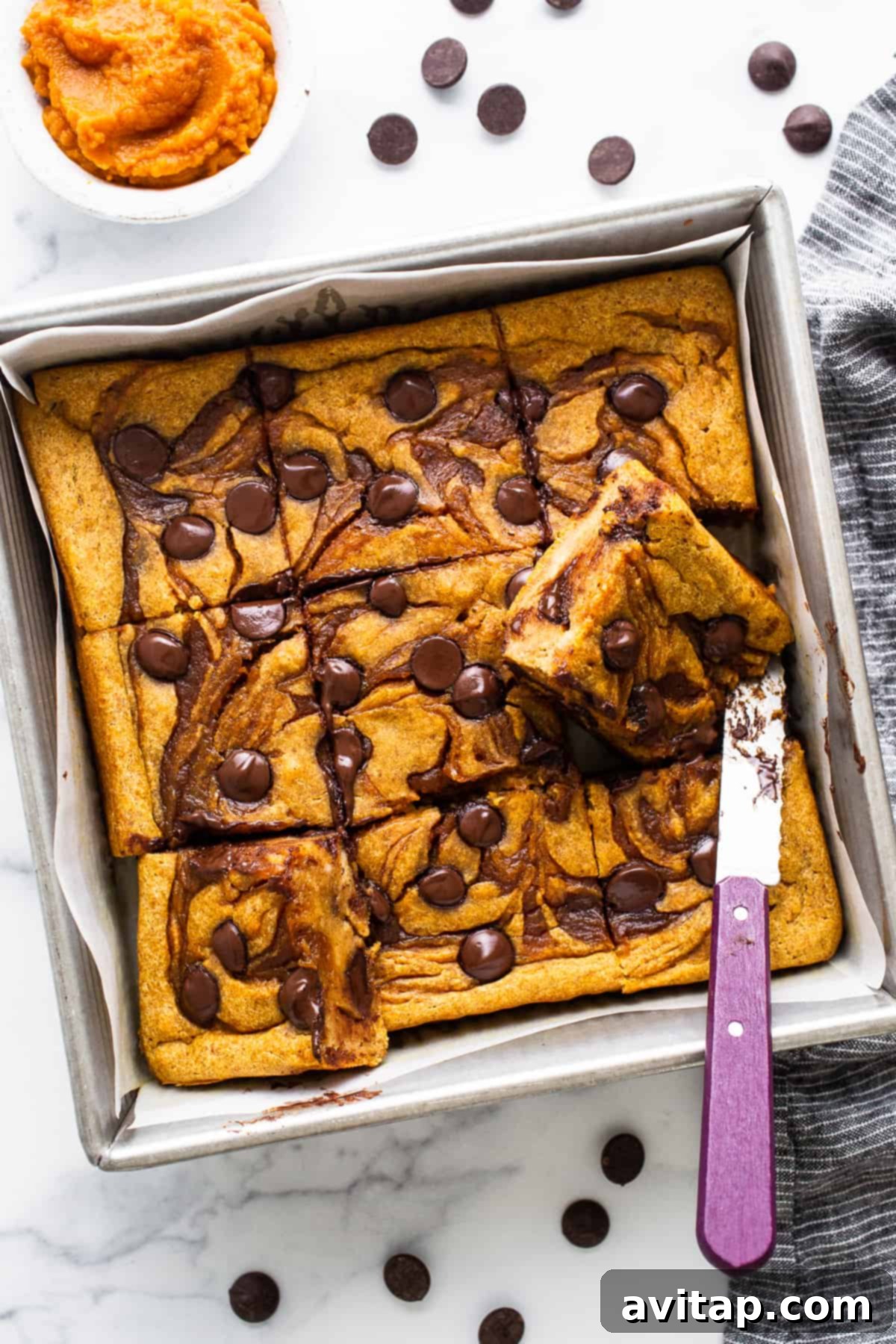 Freshly baked pumpkin chocolate chip bars in a baking pan, ready to be served, with a knife resting beside them.