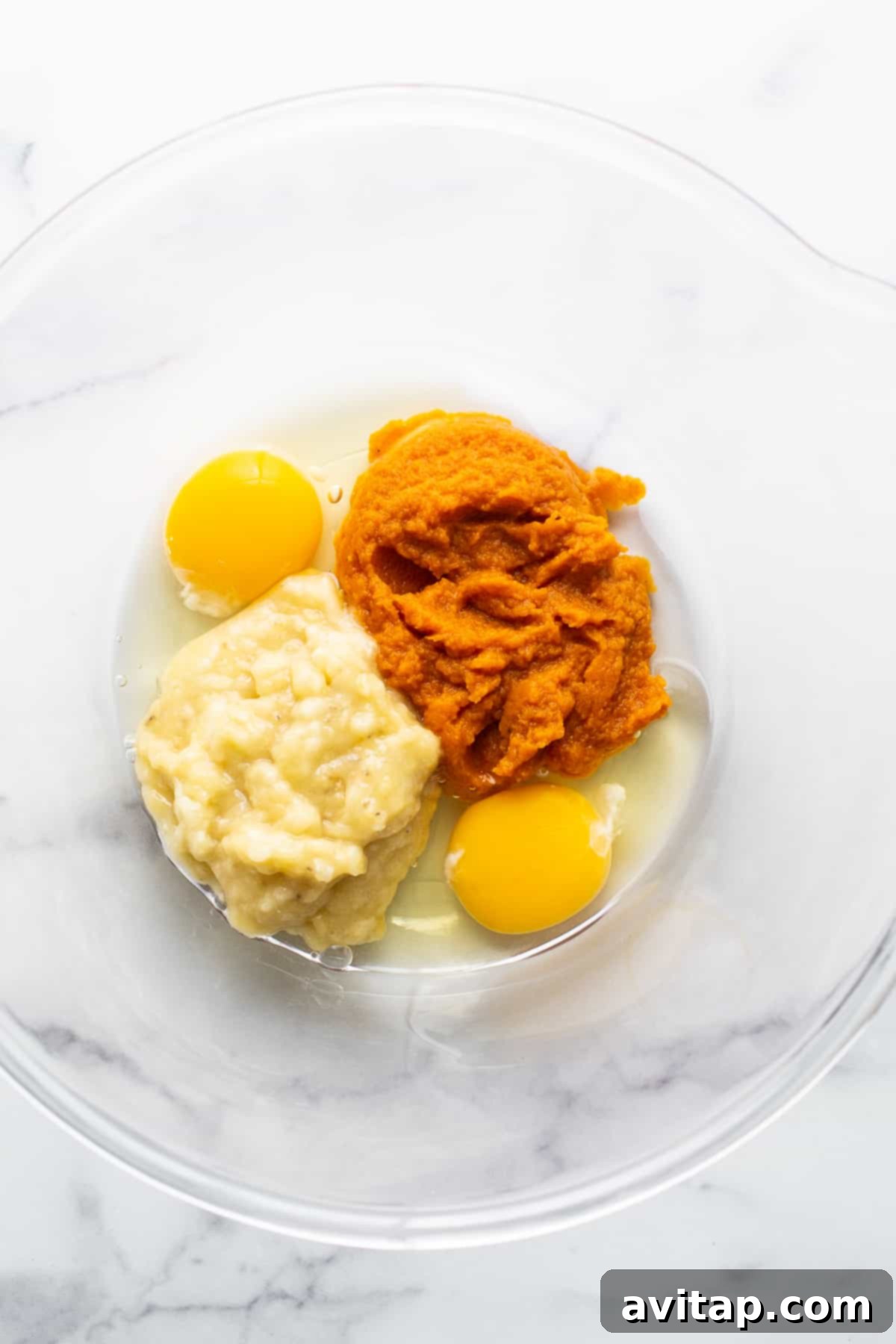 Two fresh eggs alongside a bowl of mashed sweet potato, ready for baking.