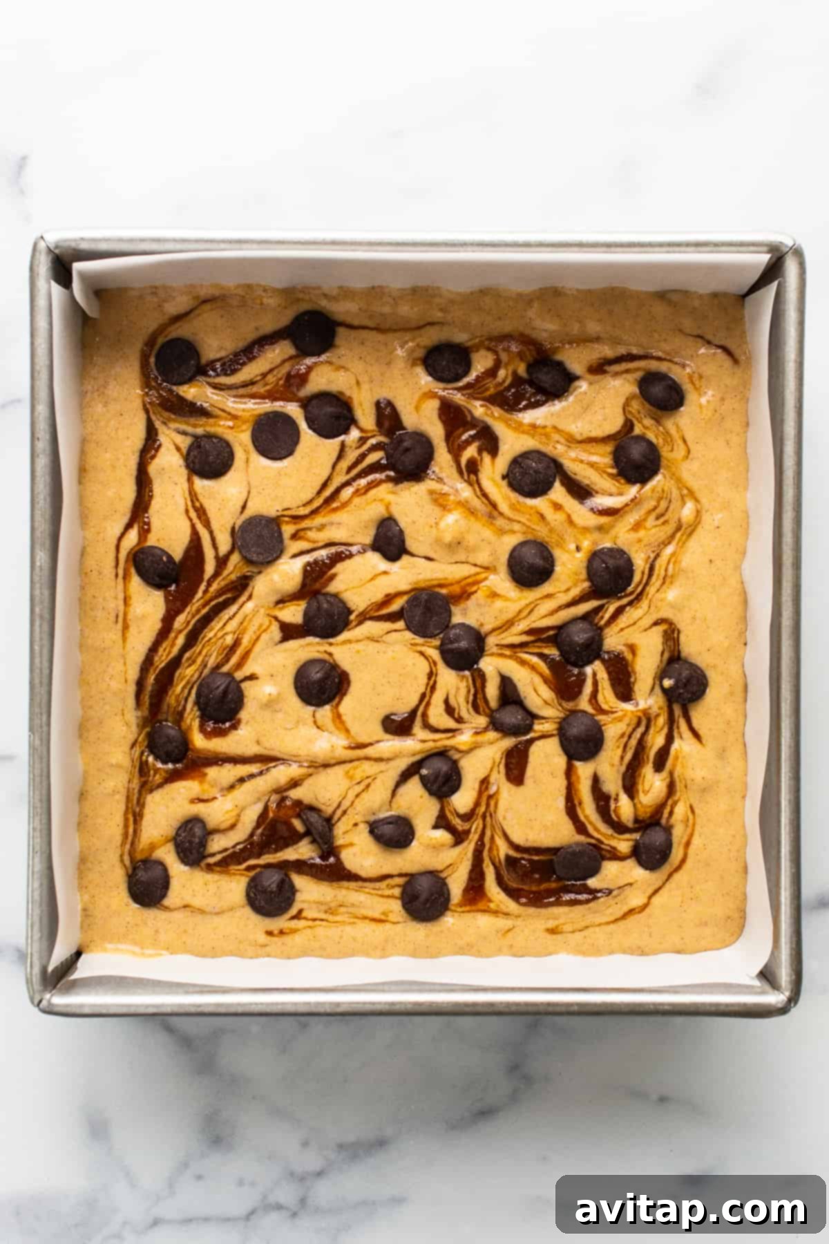A delectable brownie or cake bar with chocolate chips and a drizzle of caramel sauce in a baking pan.