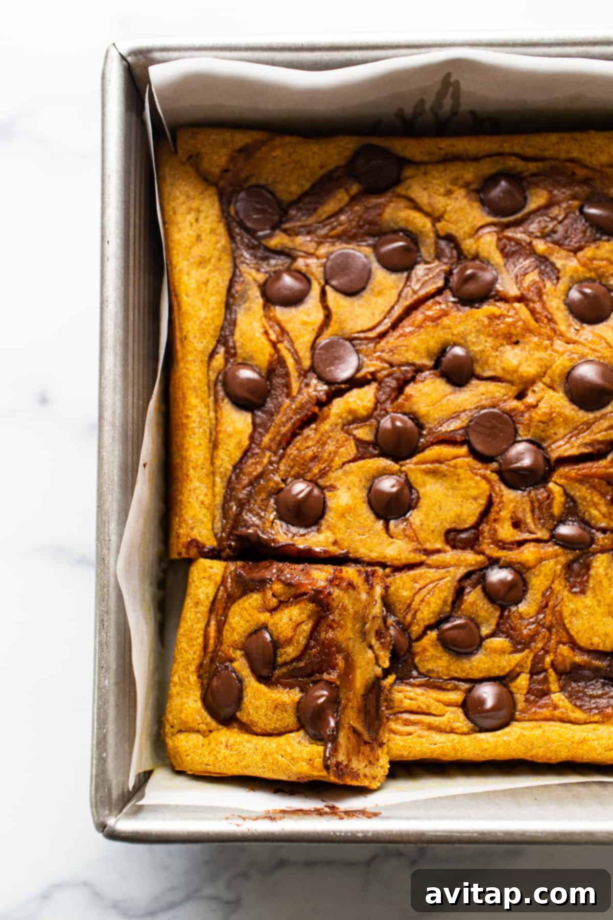 Delicious pumpkin cheesecake bars in a baking pan, garnished with chocolate chips.