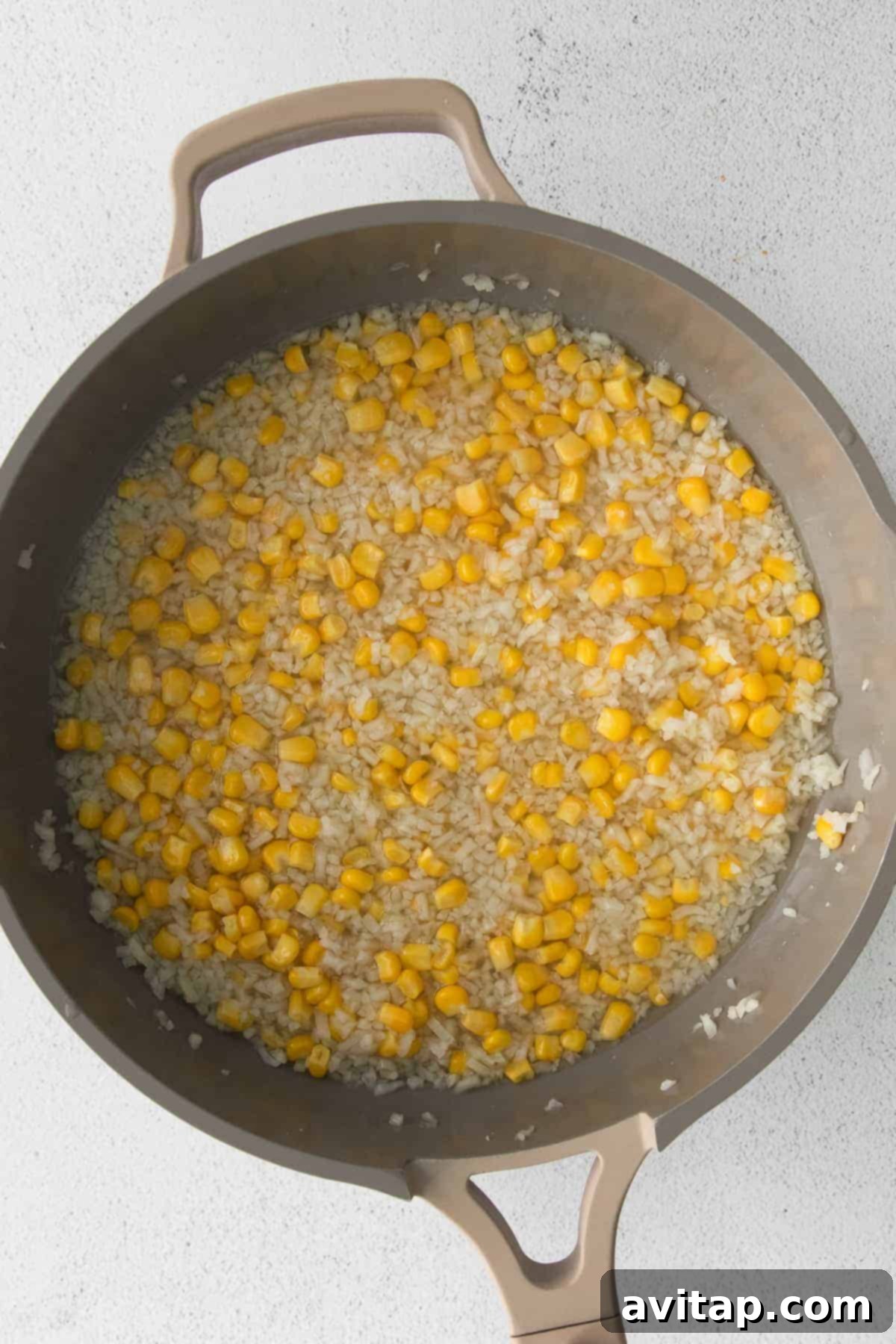 Close-up of riced cauliflower and frozen corn in a skillet, showcasing the key vegetable ingredients.