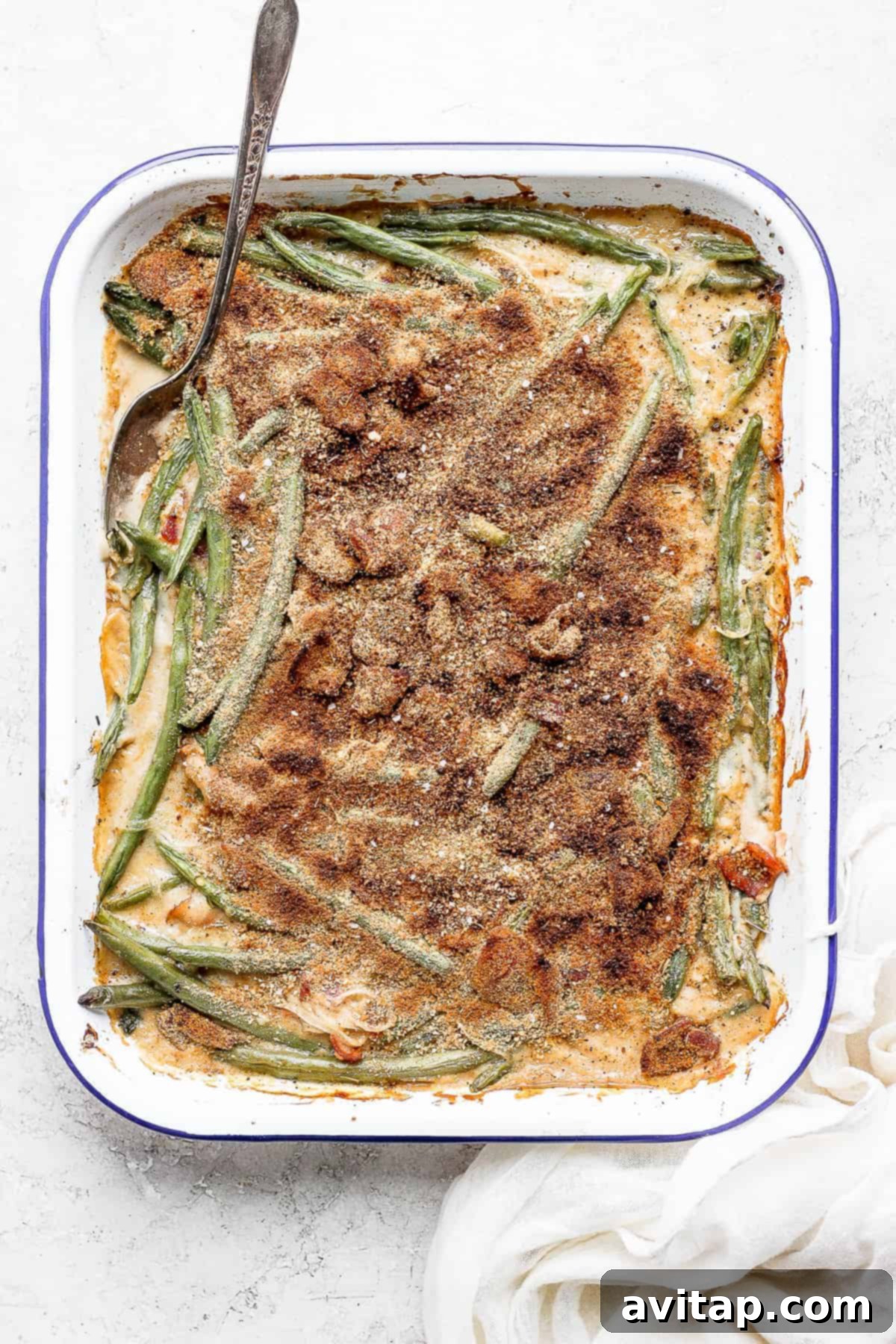 A delicious green bean casserole with crispy bacon in a white baking dish, ready to be served, with a spoon resting inside.