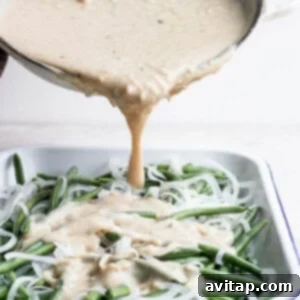 A sauce being poured over green beans in a white dish.
