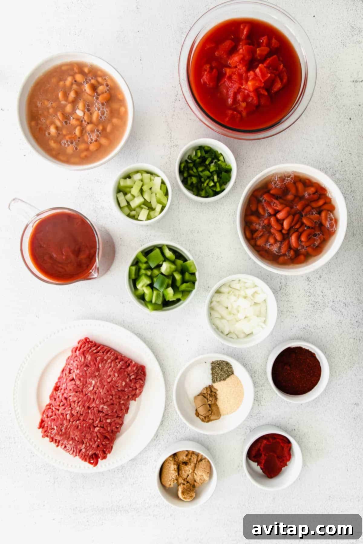 Various fresh ingredients, including ground beef, beans, and vegetables, laid out on a kitchen counter for making homemade chili.