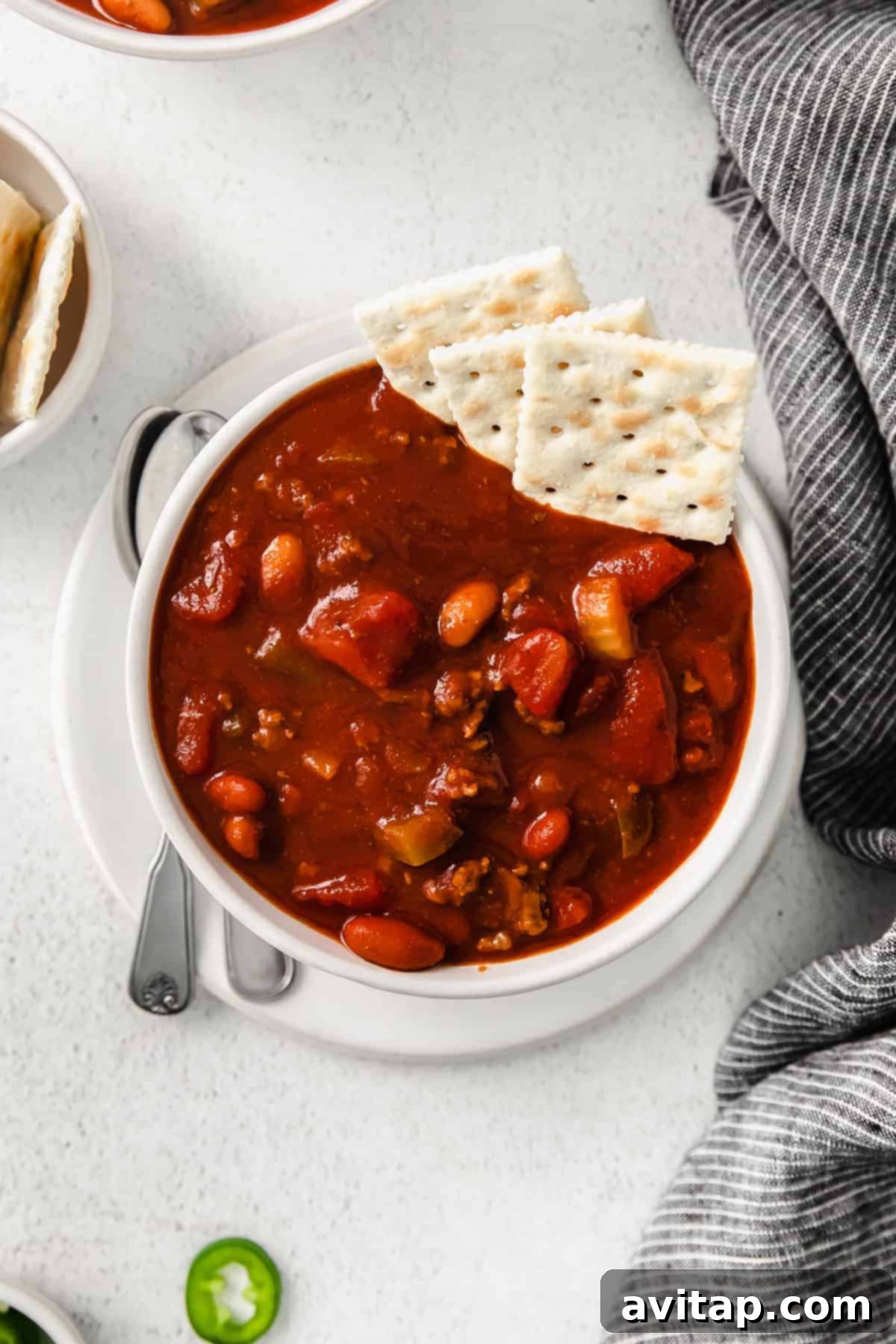 A generously sized bowl of homemade Wendy's chili, accompanied by a spoon and crackers for serving.