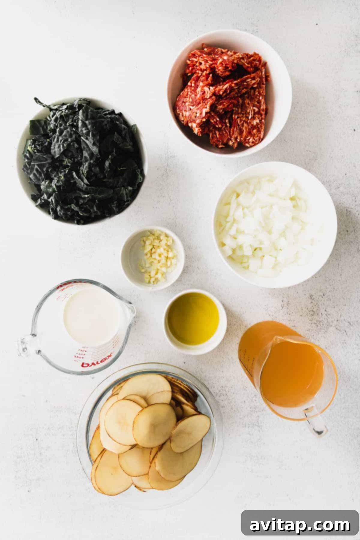 A vibrant selection of fresh ingredients laid out in small bowls, including ground Italian sausage, thinly sliced russet potatoes, chopped kale, diced white onion, and heavy cream, all perfectly prepped for cooking homemade Zuppa Toscana soup.
