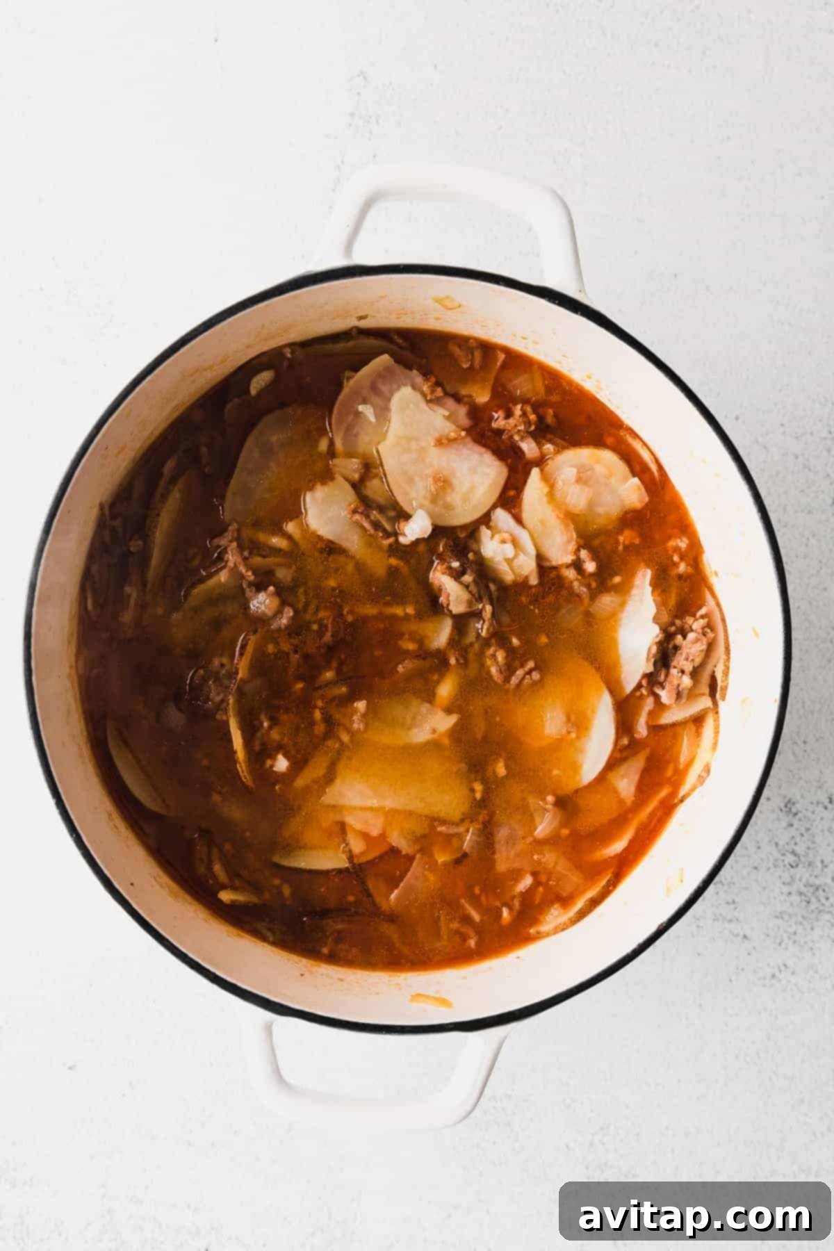 A large stockpot filled with Zuppa Toscana soup, simmering gently on a stovetop, with visible pieces of browned sausage, tender potatoes, and vibrant kale in a creamy, aromatic broth.