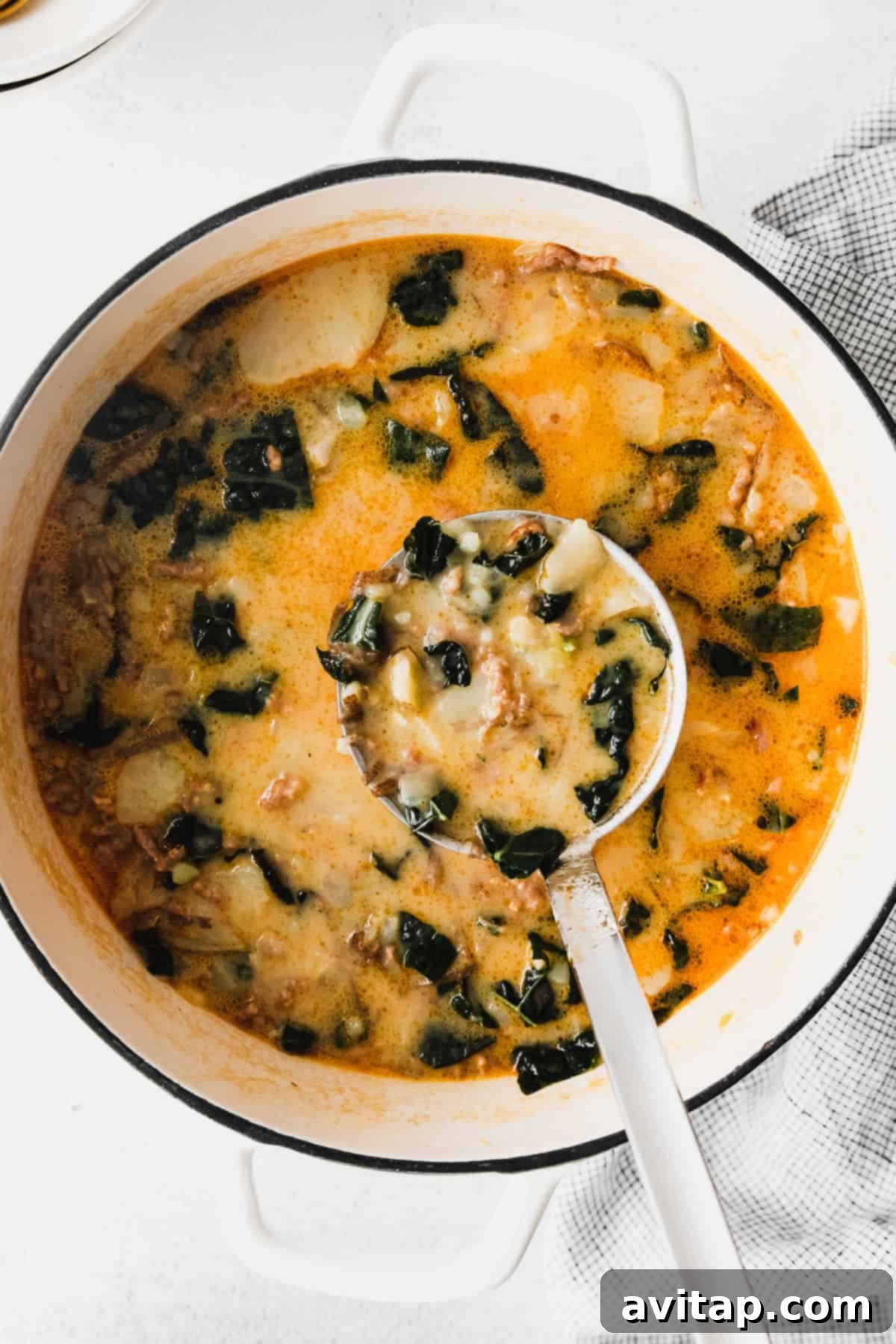 A close-up shot of a ladle dipping into a large stockpot filled with steaming Olive Garden Zuppa Toscana soup, showing the creamy broth, well-cooked pieces of sausage, and vibrant tender kale and potatoes.