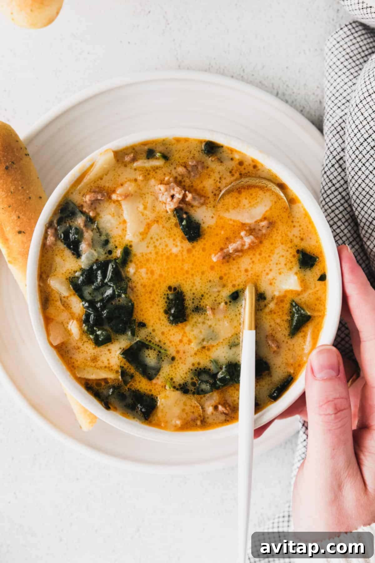 A beautiful, steaming bowl of Zuppa Toscana soup, perfectly garnished with green herbs, served elegantly with a warm, golden-brown breadstick on the side, inviting you to a comforting meal.