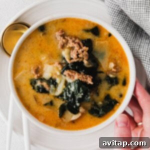 A person holding a bowl of Zuppa Toscana soup with meat and greens, freshly made and ready to eat.