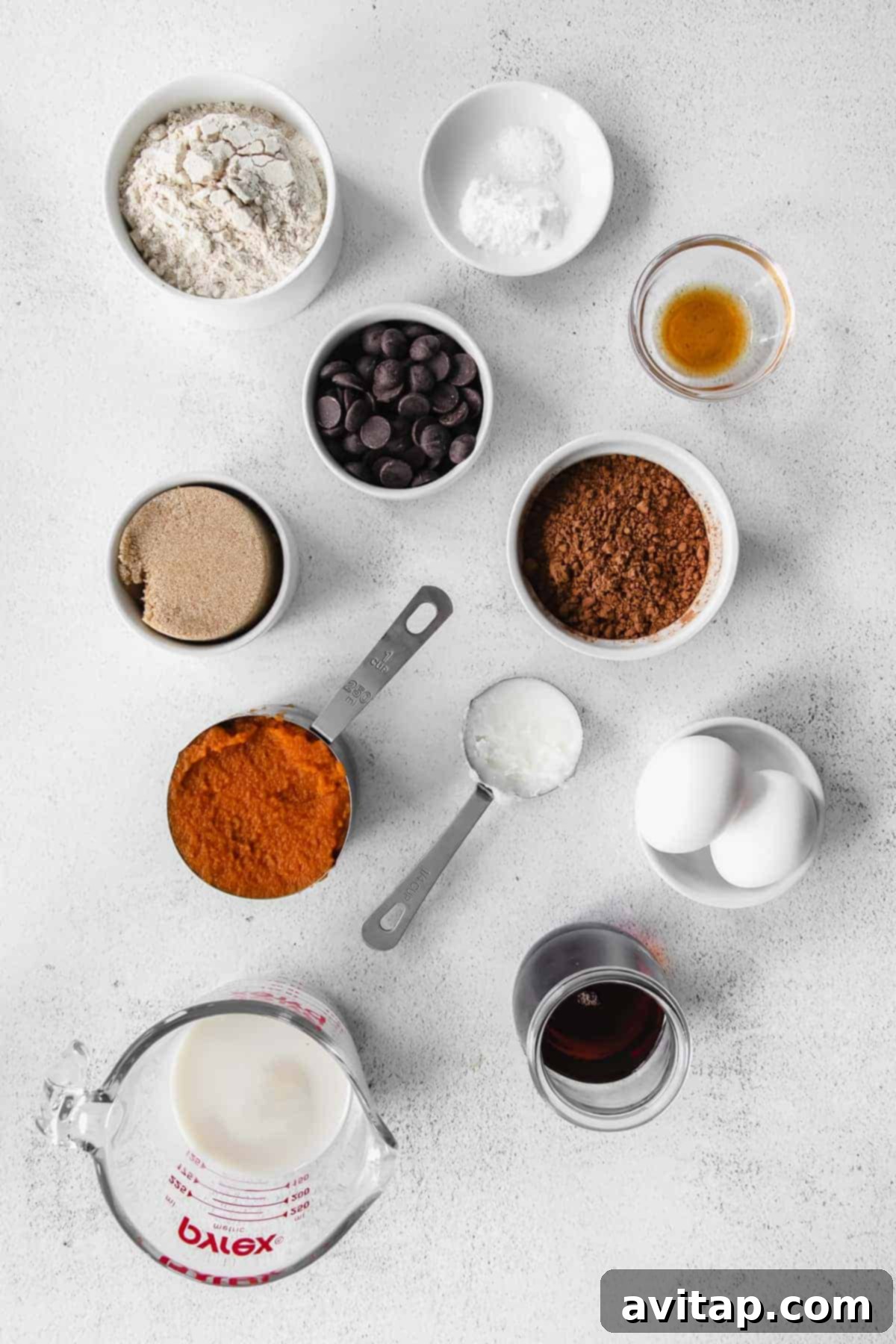 A collection of ingredients for chocolate pumpkin bread neatly arranged in small bowls, ready for baking.