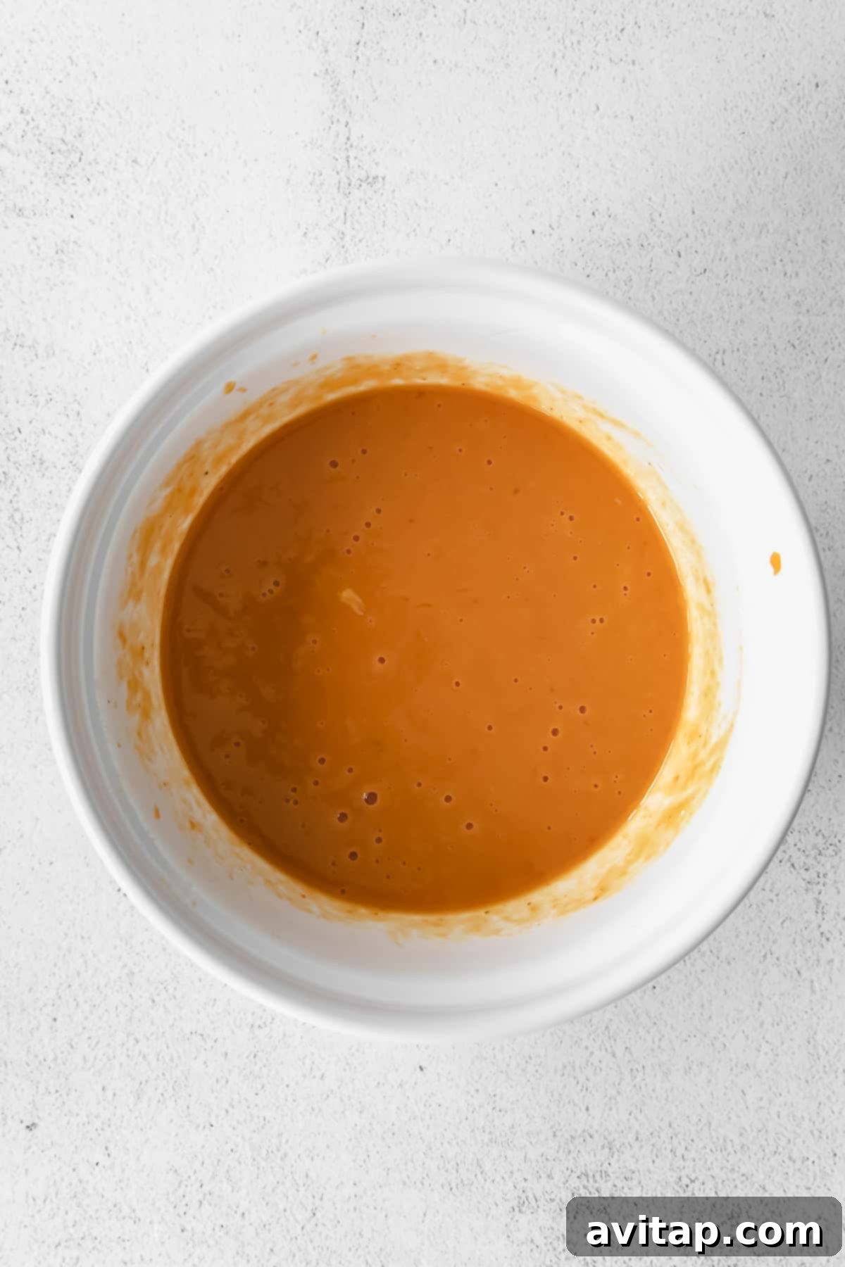 Wet ingredients for pumpkin bread, including pumpkin puree, milk, and eggs, fully mixed in a bowl.