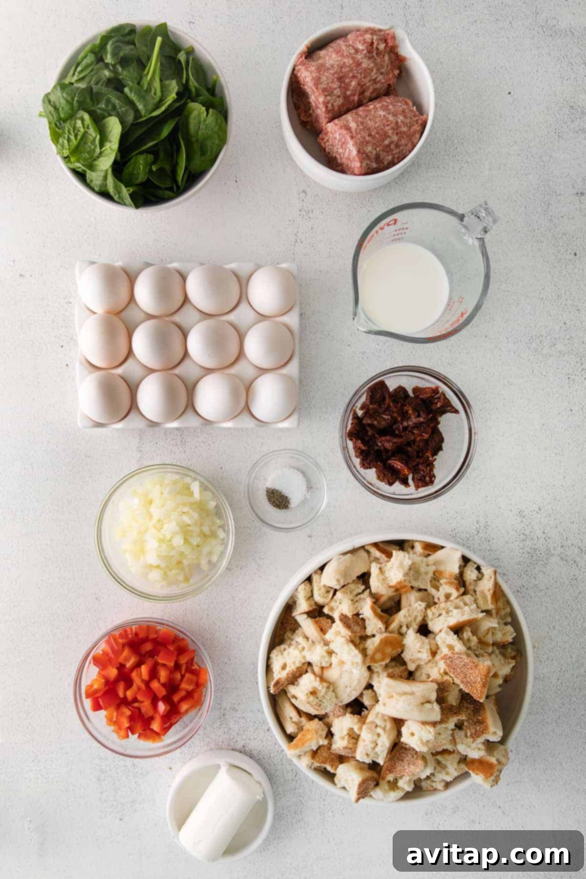 A vibrant selection of breakfast bake ingredients: sausage, eggs, sun-dried tomatoes, milk, bell peppers, and spinach.
