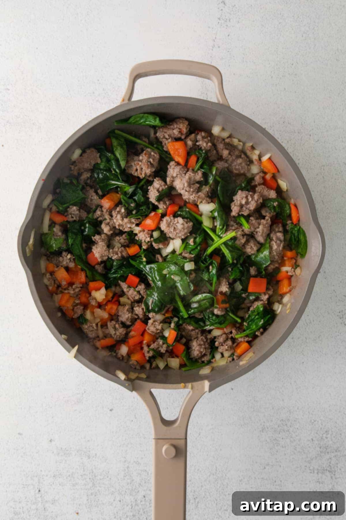 Sautéed sausage, onion, bell peppers, and spinach cooking in a skillet, filling the kitchen with enticing aromas.