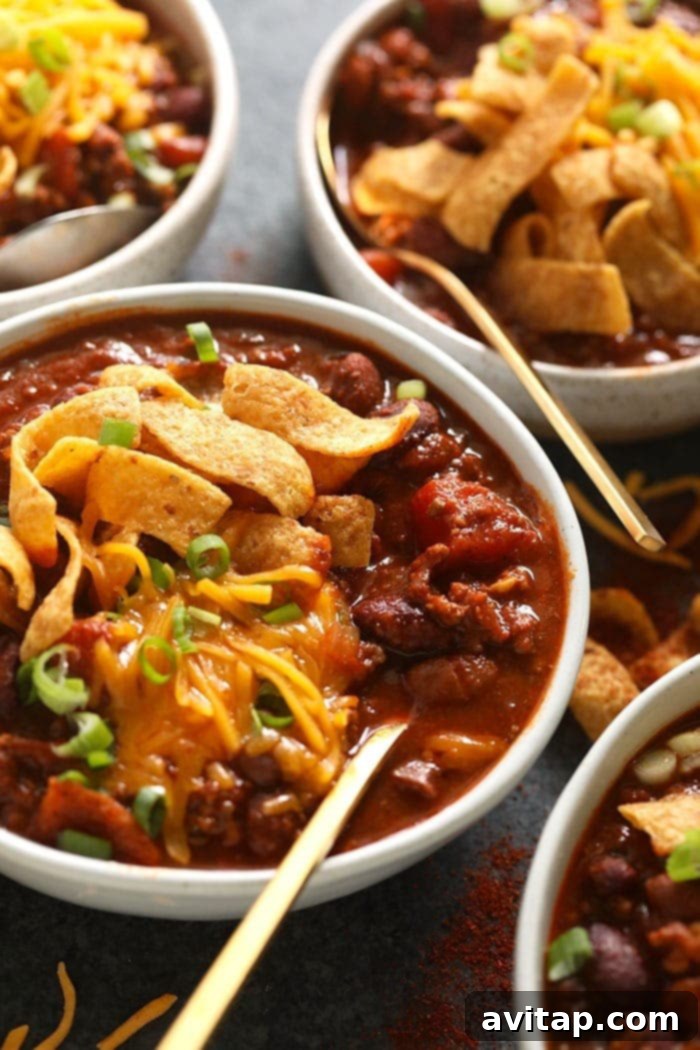 A close-up of a bowl of rich beef chili, garnished with crispy Fritos and a generous sprinkle of shredded cheese, inviting you to dig in.