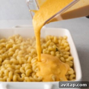 Creamy butternut squash mac and cheese being transferred into a baking dish for broiling.