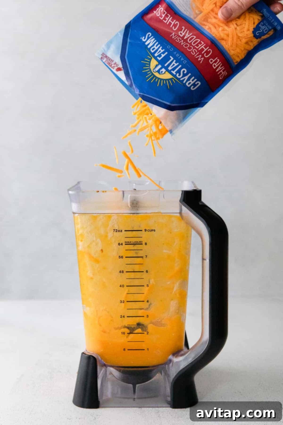 Shredded cheddar cheese being added to a blender, ready to be incorporated into the creamy butternut squash sauce.