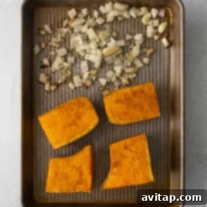Roasted butternut squash and sweet potato slices on a baking sheet, with garlic and onion.