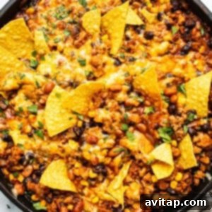 A skillet of baked nachos with melted cheese, ground meat, beans, and corn, garnished with crispy tortilla chips.