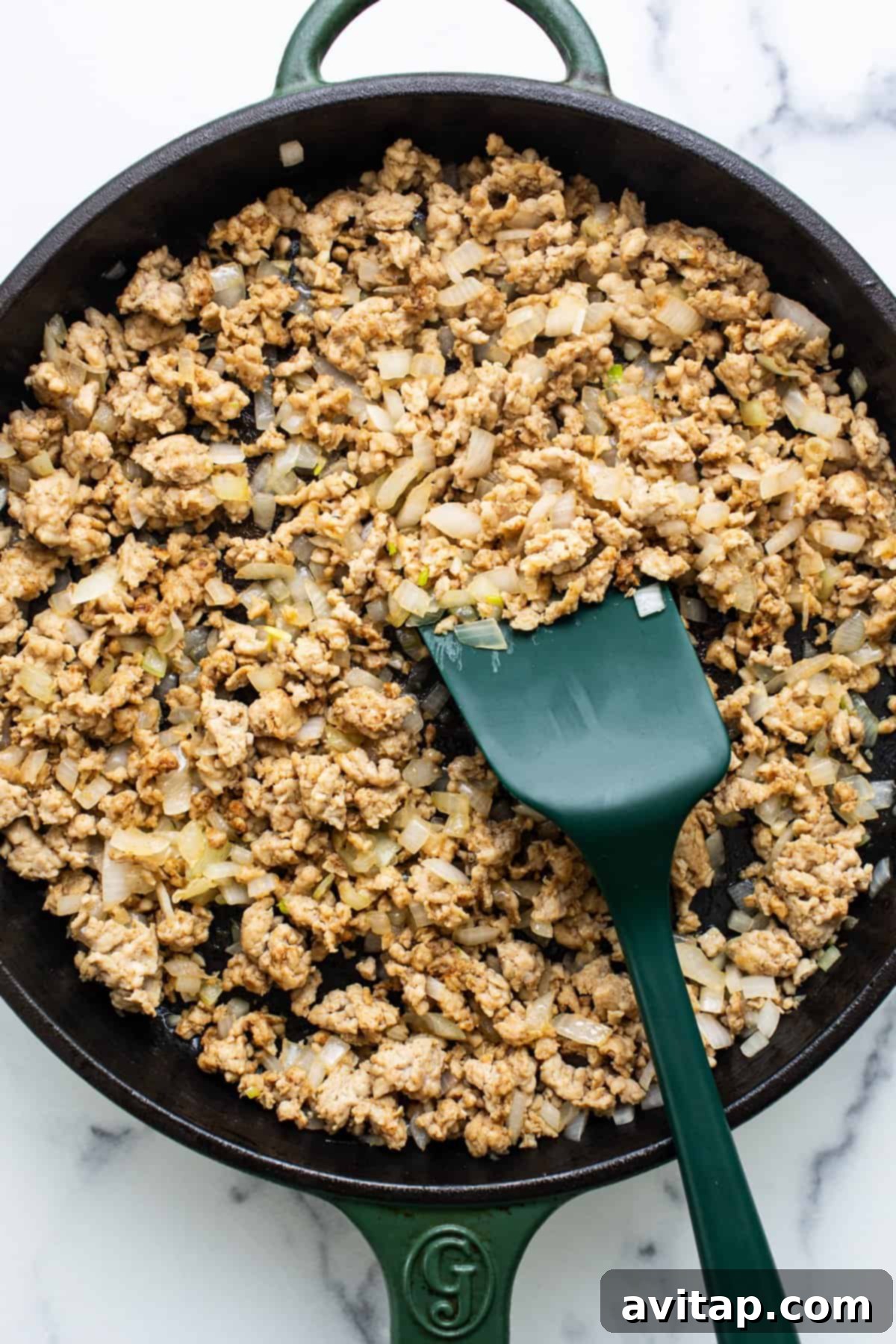Ground meat cooked with diced onions in a cast iron skillet, with a green spatula.