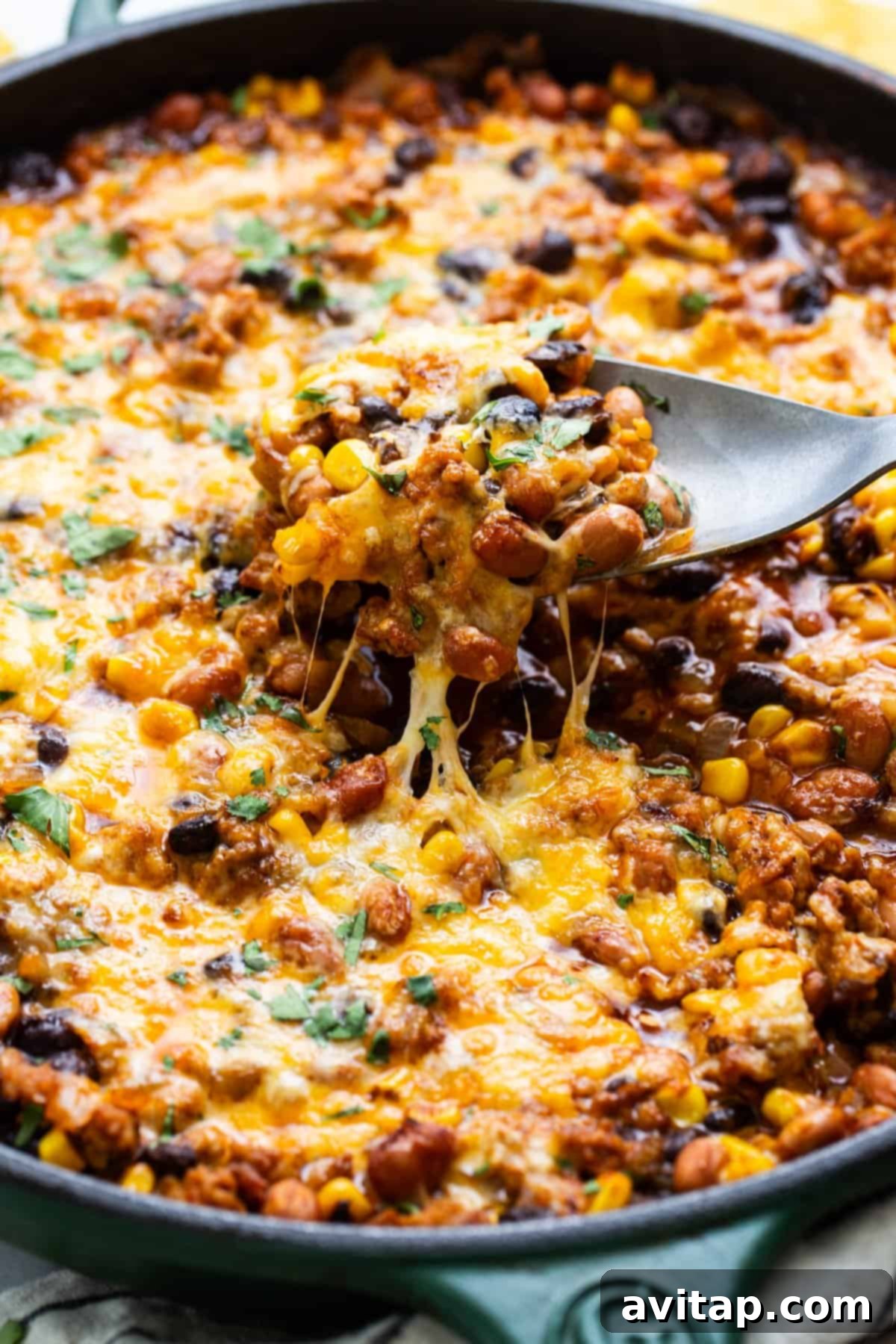 Skillet of baked cheesy chili with a spoon lifting a portion showing melted cheese stretch.
