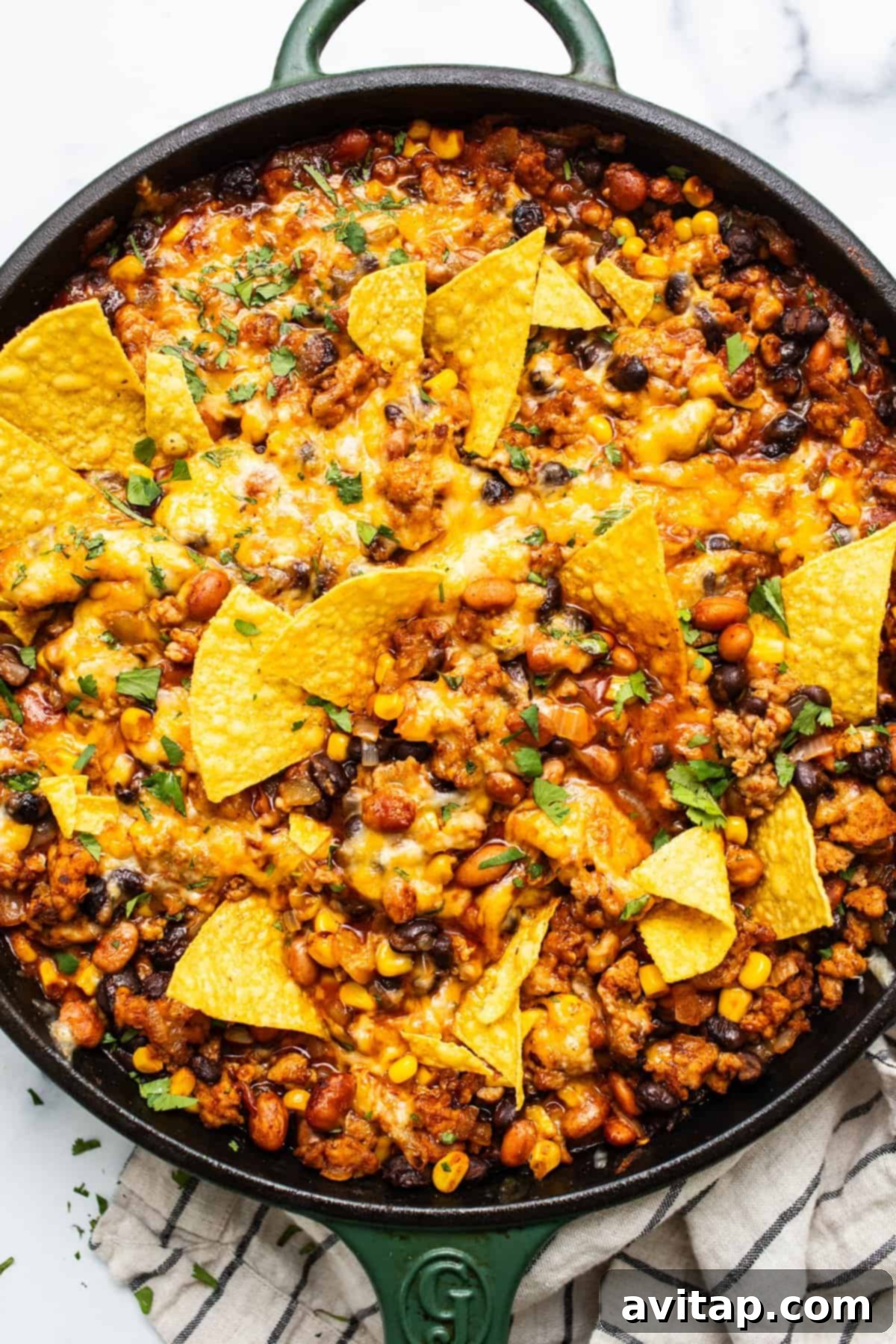 A skillet of baked nachos with melted cheese, ground meat, beans, and corn, garnished with crispy tortilla chips.