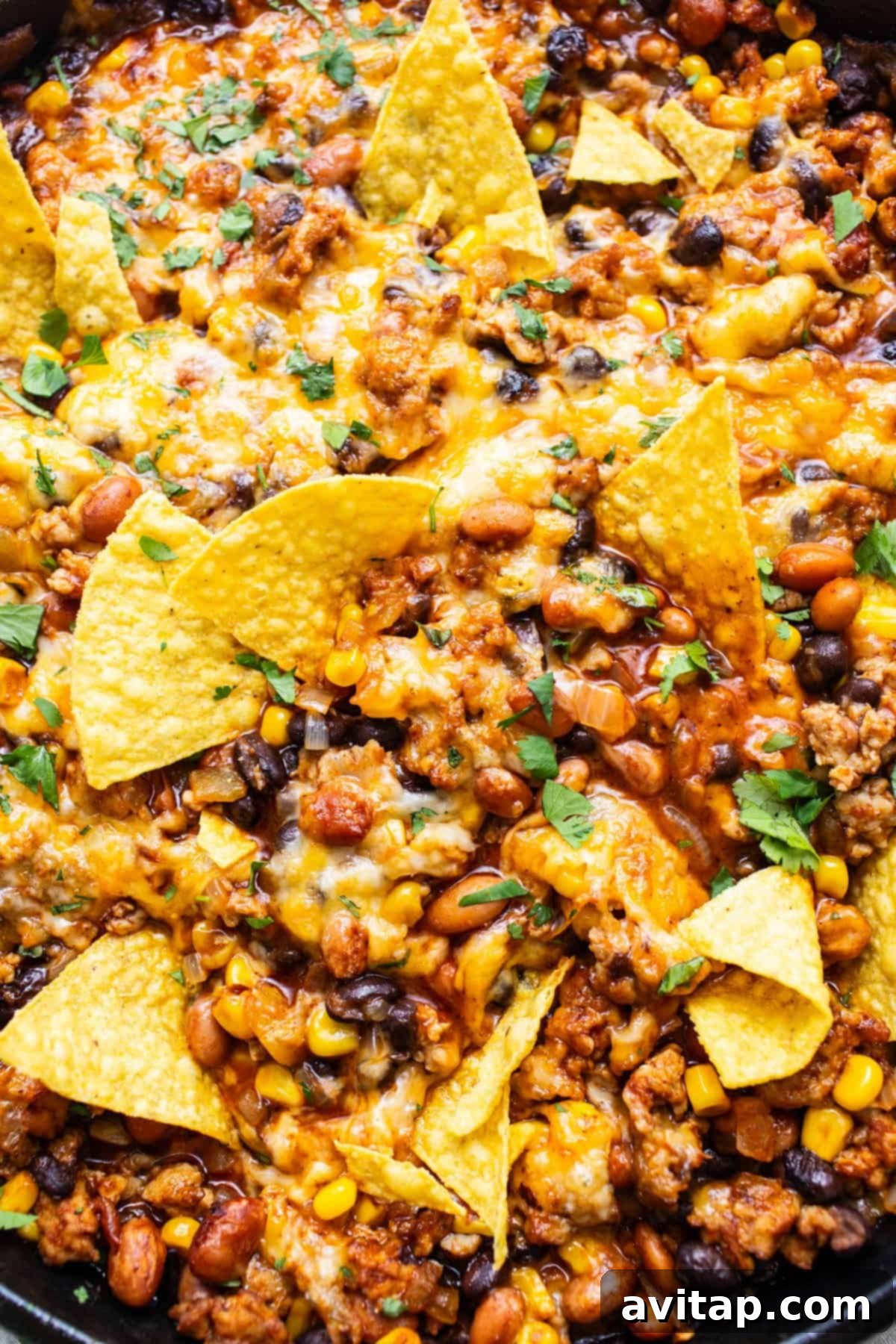 A skillet with nachos covered in melted cheese, ground meat, beans, corn, and garnished with fresh herbs.