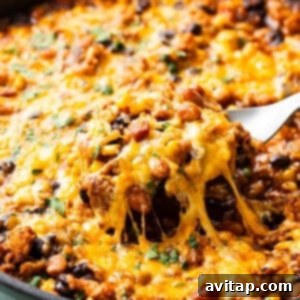 A skillet with melted cheese being lifted, revealing a cheesy, bean and meat mixture beneath.