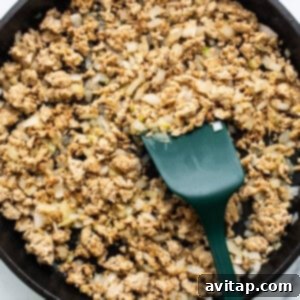 Ground meat cooked with diced onions in a cast iron skillet, with a green spatula.