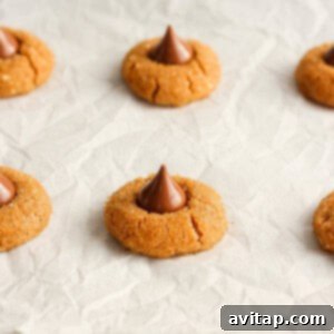 Warm peanut butter cookies with chocolate kisses being pressed onto a baking sheet.