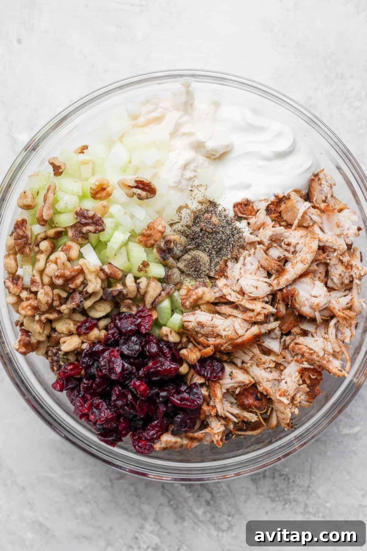 A mixing bowl filled with creamy turkey salad ingredients, showing visible pieces of turkey, cranberries, and walnuts, ready for chilling.