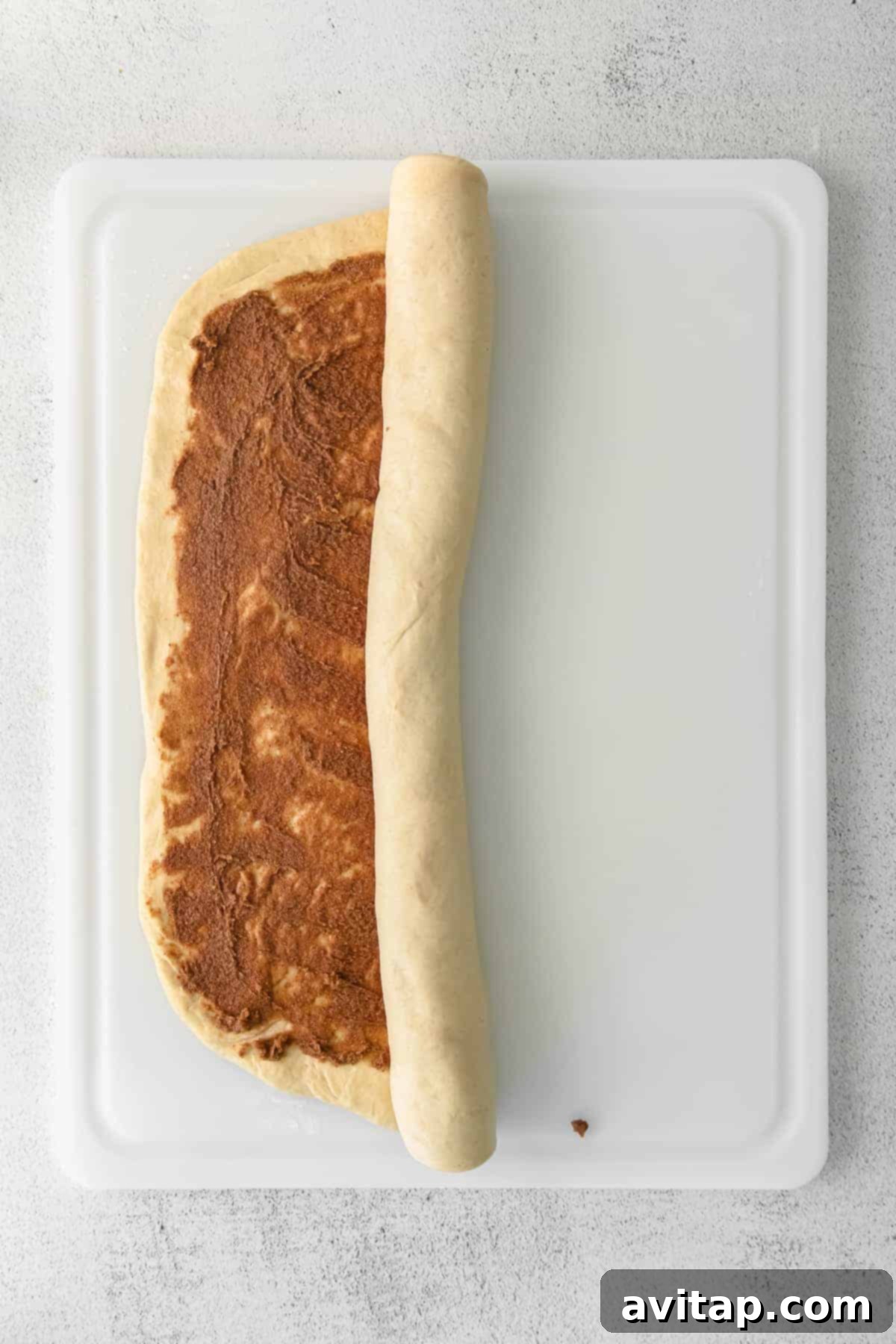 maple cinnamon roll dough being rolled into a tight log with filling